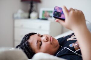 Adolescent allongé sur son lit, absorbé par son smartphone, illustrant l'addiction aux écrans