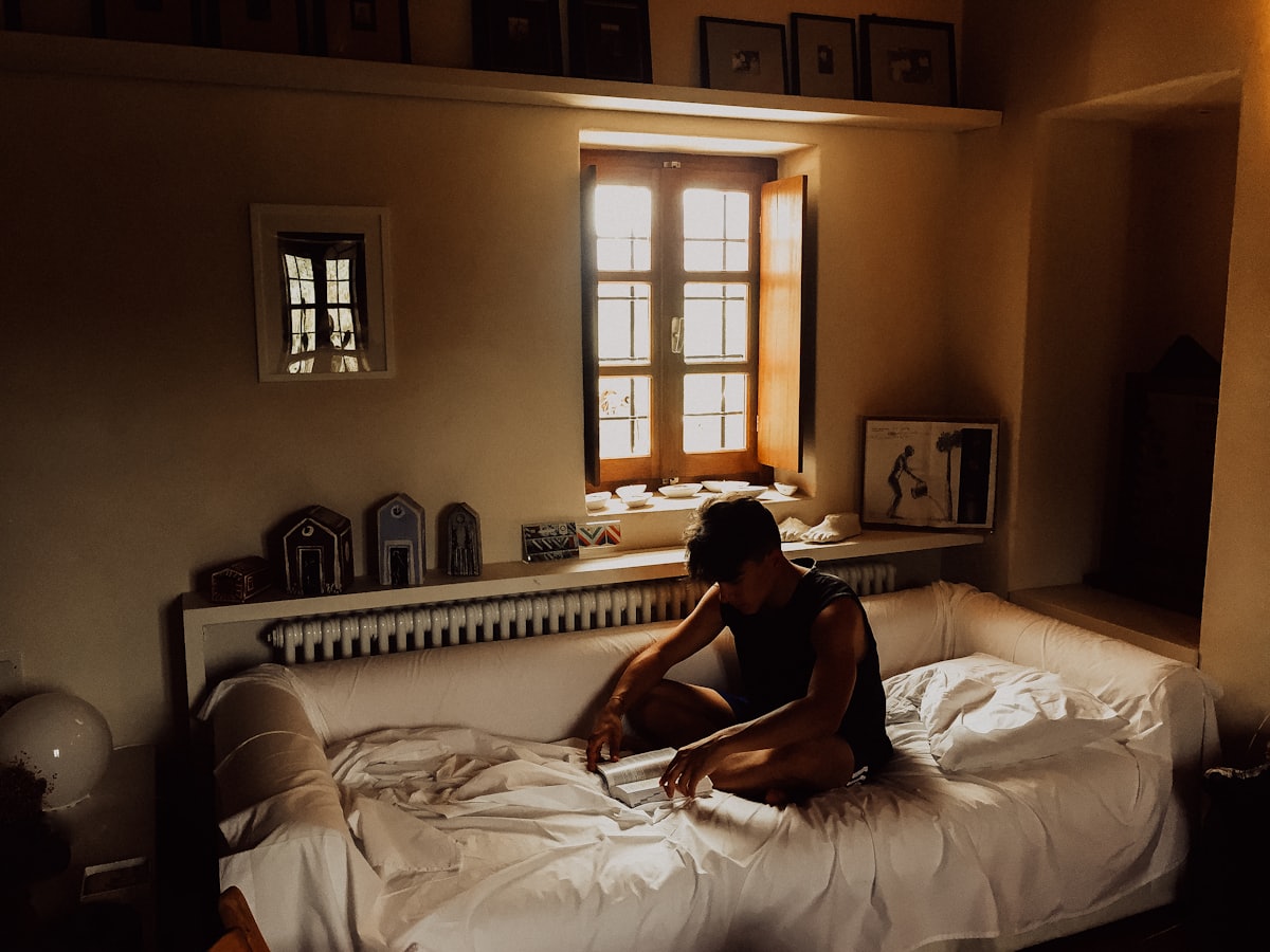 Personne assise au bord du lit dans une chambre sombre aux volets mi-clos, illustrant les signes de dépression à surveiller