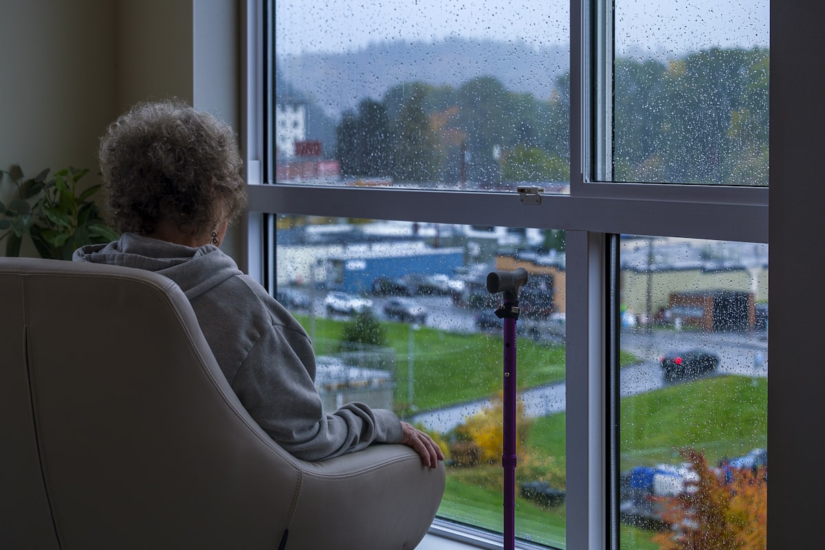 Rumination et inquiétude diffuse Personne assise dans un fauteuil qui rumine ses inquiétudes devant une fenêtre sous la pluie, illustrant les symptômes de l'anxiété généralisée