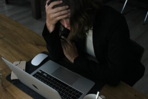 Femme submergée par la charge mentale, tête dans les mains devant son ordinateur