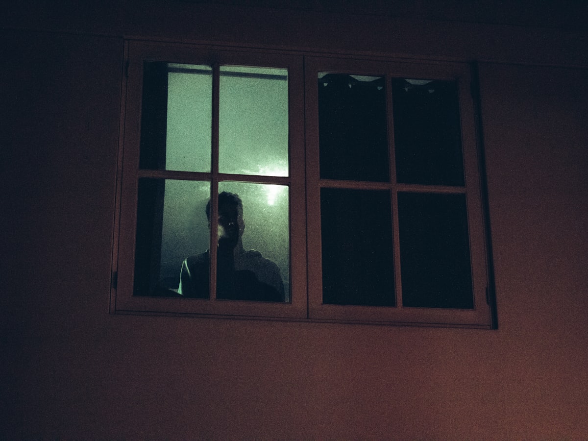 Signes de dépression chez l'homme Silhouette d'un homme à sa fenêtre la nuit, évoquant les signes de dépression chez l'homme