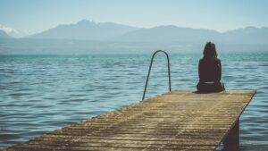 امرأة تجلس وحيدة على طرف رصيف خشبي أمام بحيرة، صورة تعبّر عن الوحدة