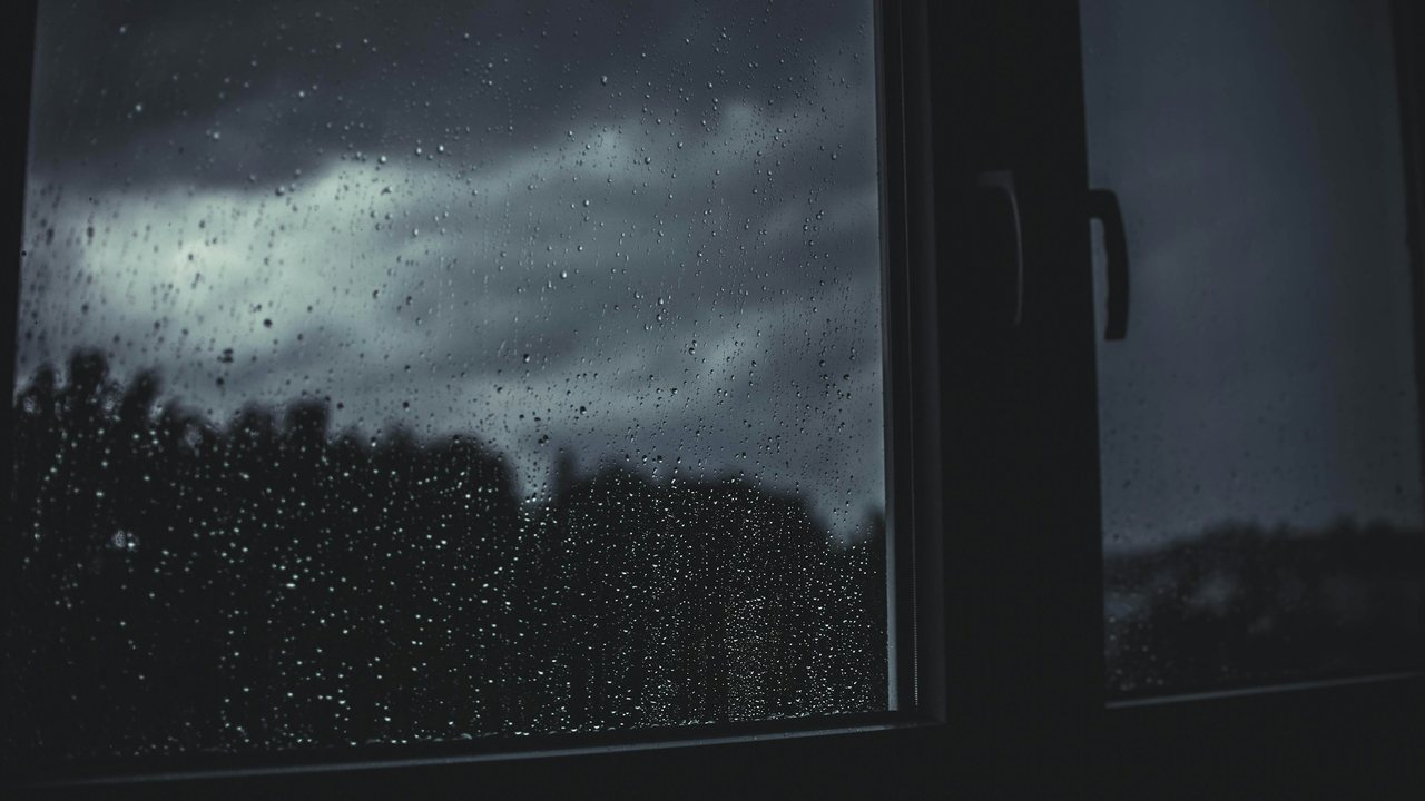 Fenêtre couverte de gouttes de pluie sous un ciel gris : les jours sombres de la dépression saisonnière