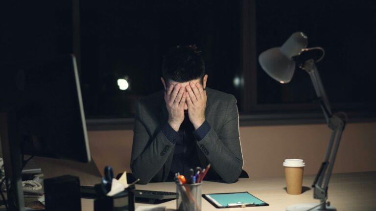 Salarié seul à son bureau le soir, la tête dans les mains : l'épuisement que provoque le harcèlement moral au travail
